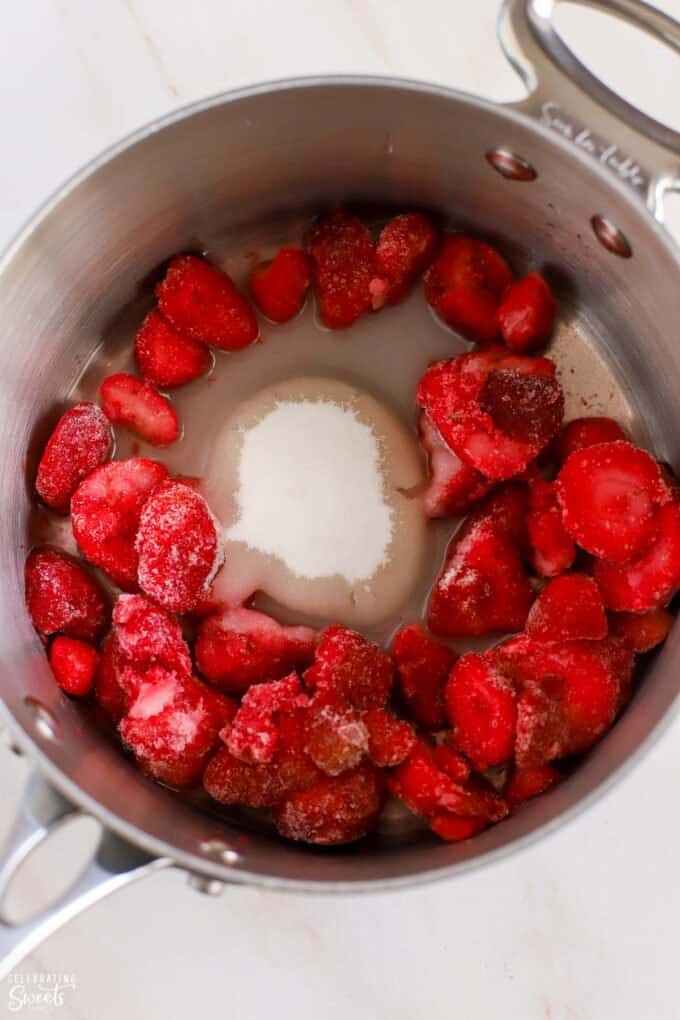 Frozen strawberries, sugar, and water in a saucepan.