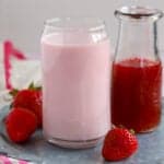 Glass of strawberry milk and a carafe of strawberry syrup.