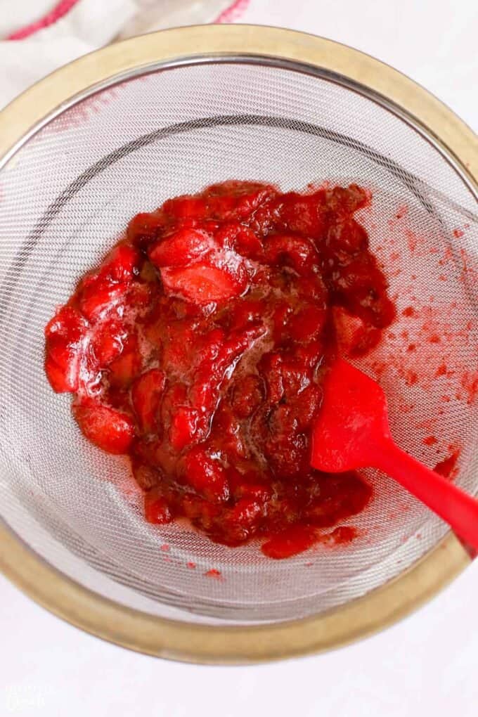 Cooked strawberries in a fine mesh sieve over a bowl.