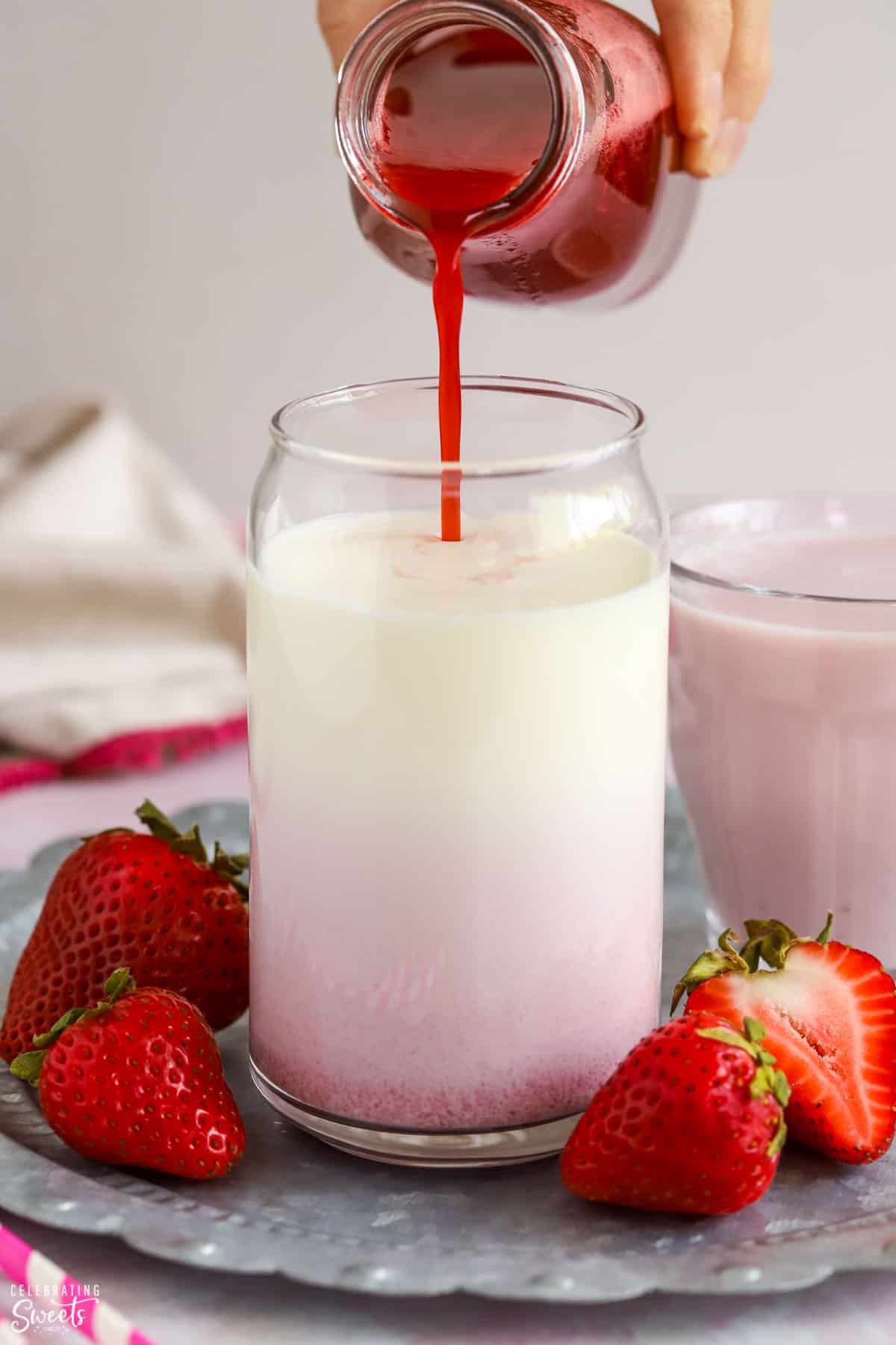 Strawberry syrup being poured into a glass of milk.