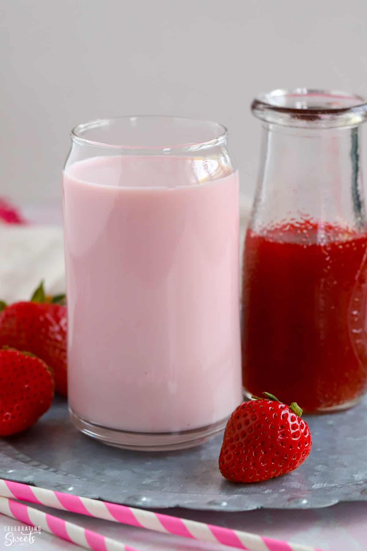 Glass of strawberry milk and a carafe of strawberry syrup.