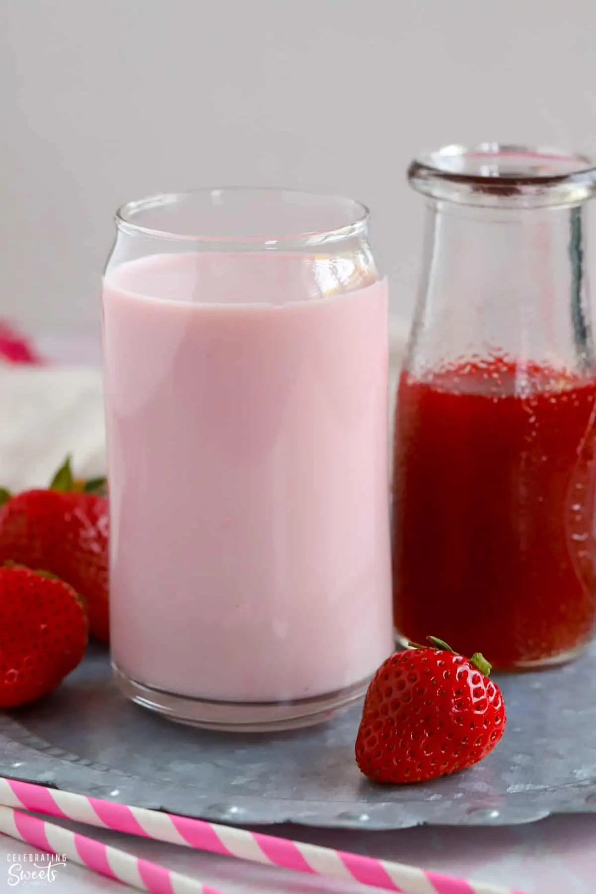 Glass of strawberry milk and a carafe of strawberry syrup.