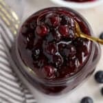 Blueberry Pie Filling in a glass jar with a gold spoon.