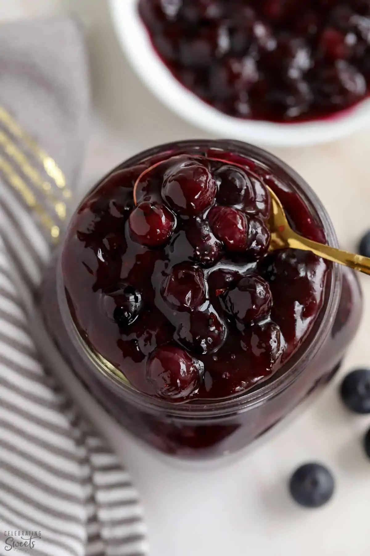Blueberry Pie Filling in a glass jar with a gold spoon.