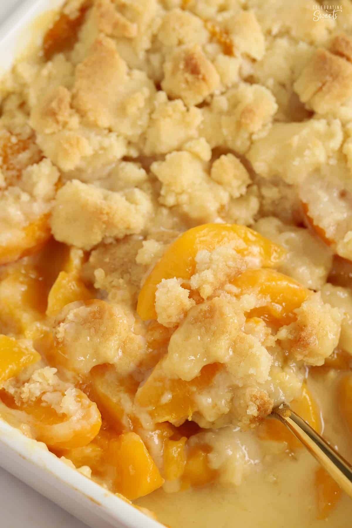 Peach cobbler in a baking dish with a gold spoon.
