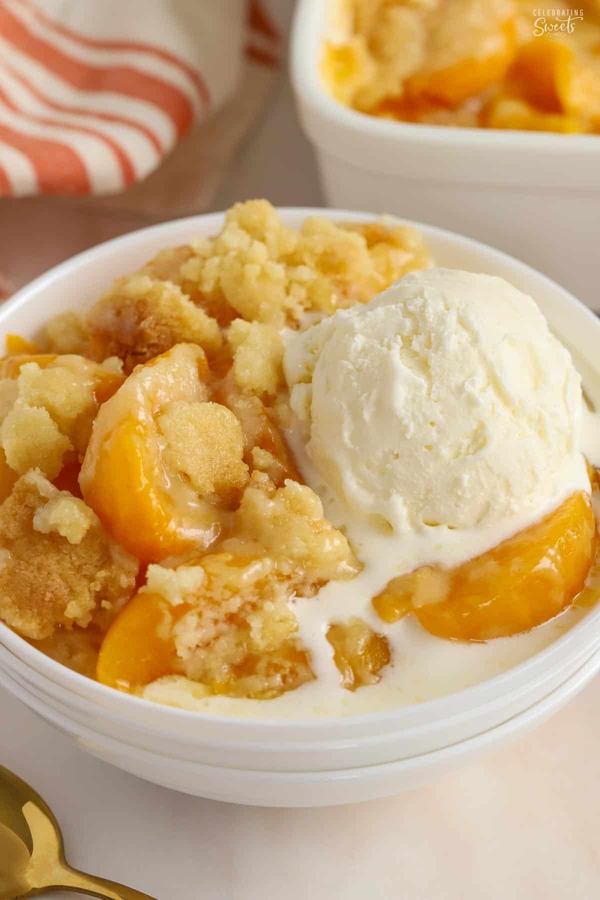 Peach cobbler in a white bowl topped with ice cream.
