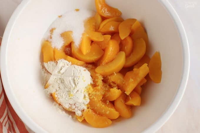 Peaches, flour, sugar, and lemon zest in a white bowl.