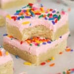 Two sugar cookie bars topped with pink frosting and sprinkles stacked on top of each other.