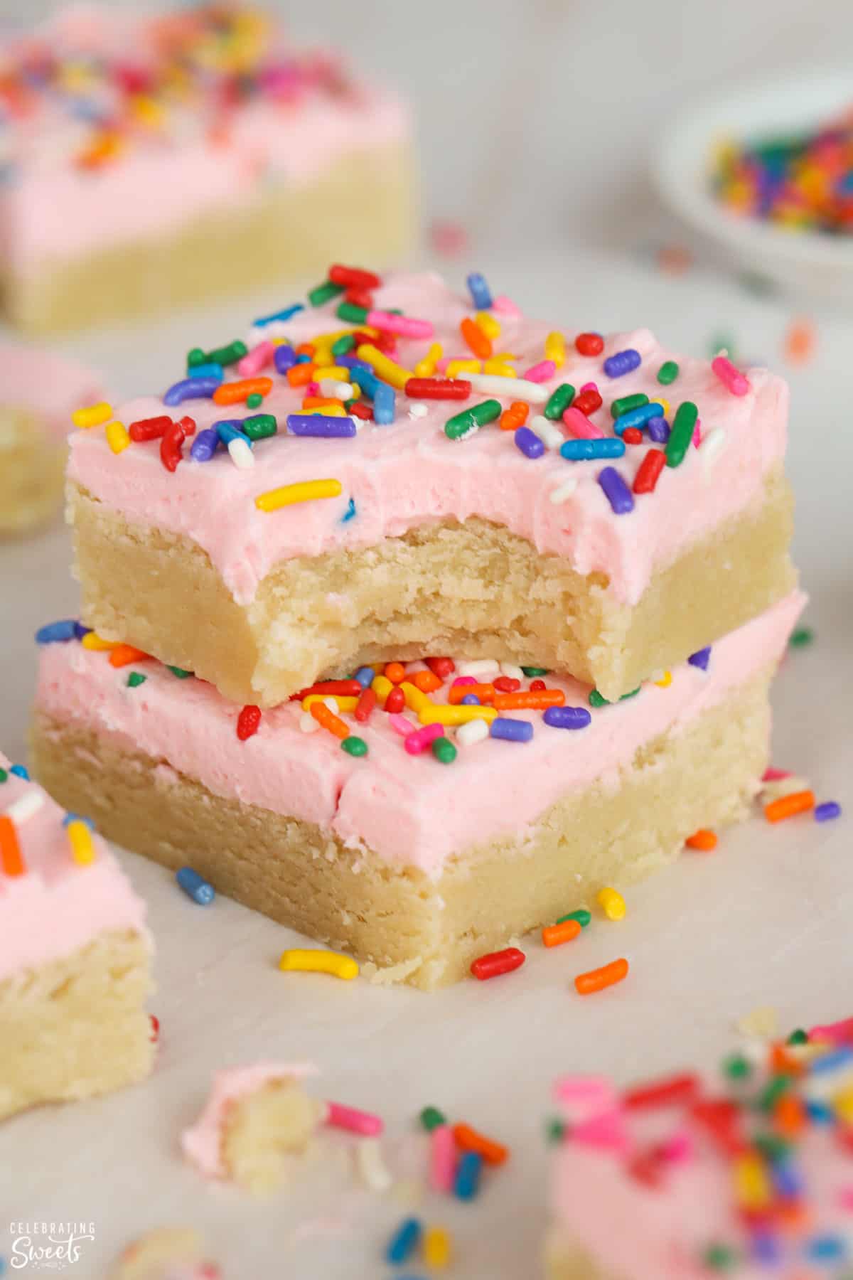 Two sugar cookie bars topped with pink frosting and sprinkles stacked on top of each other.
