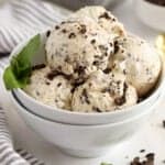 Scoops of mint chip ice cream in a white bowl garnished with fresh mint.