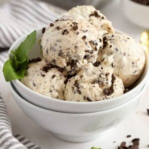Scoops of mint chip ice cream in a white bowl garnished with fresh mint.