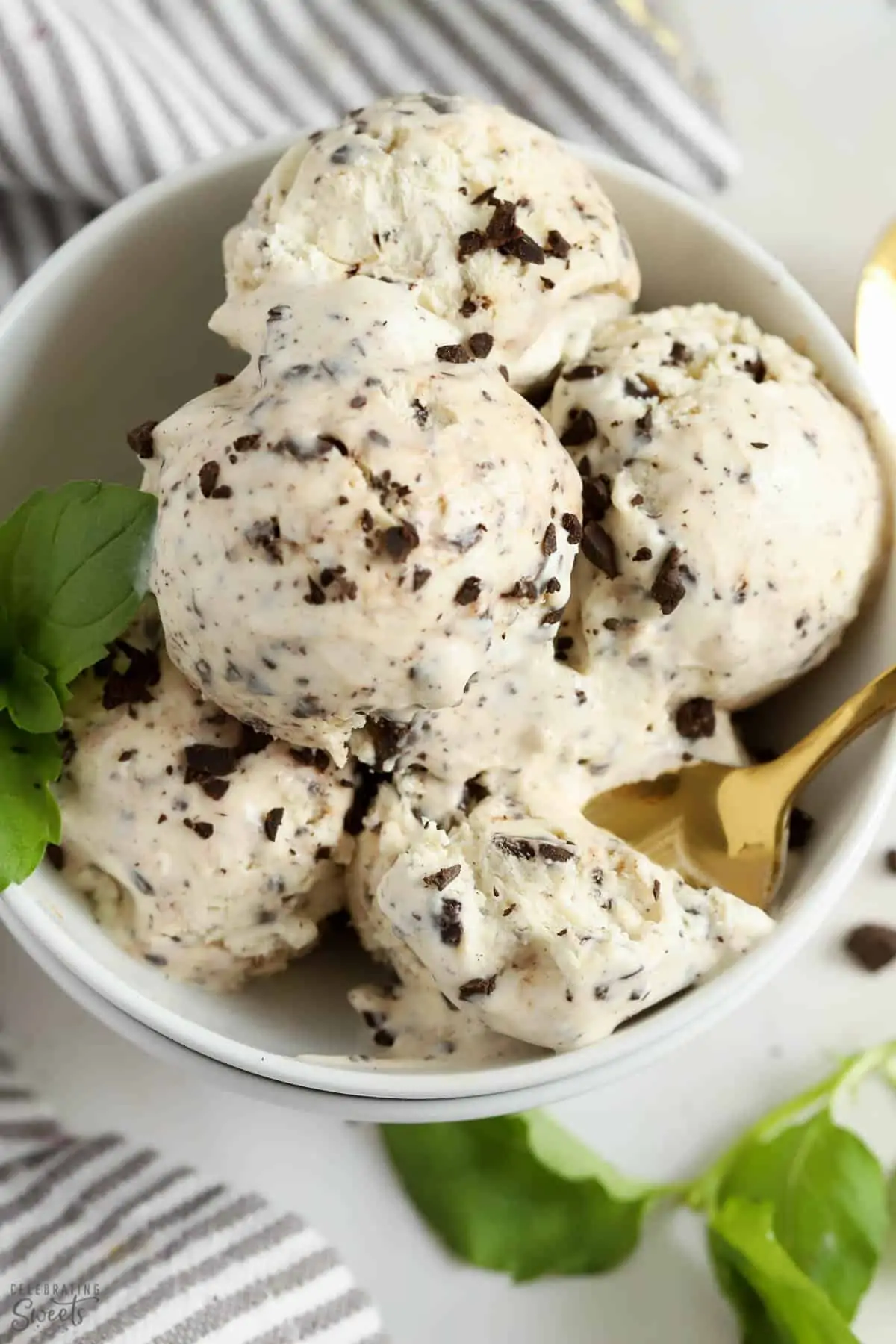 Scoops of mint chip ice cream in a white bowl garnished with fresh mint.