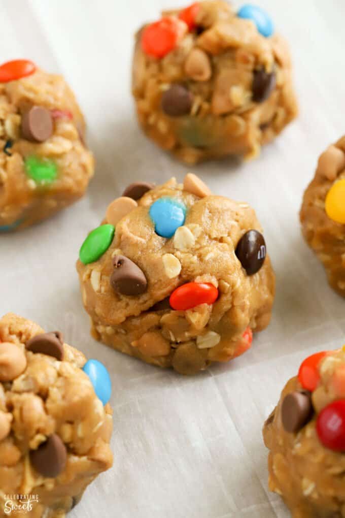 Cookie dough balls toped with M&M's and chocolate chips on a parchment lined baking sheet.