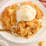 Apple crumble on a white plate topped with a scoop of melty vanilla ice cream.