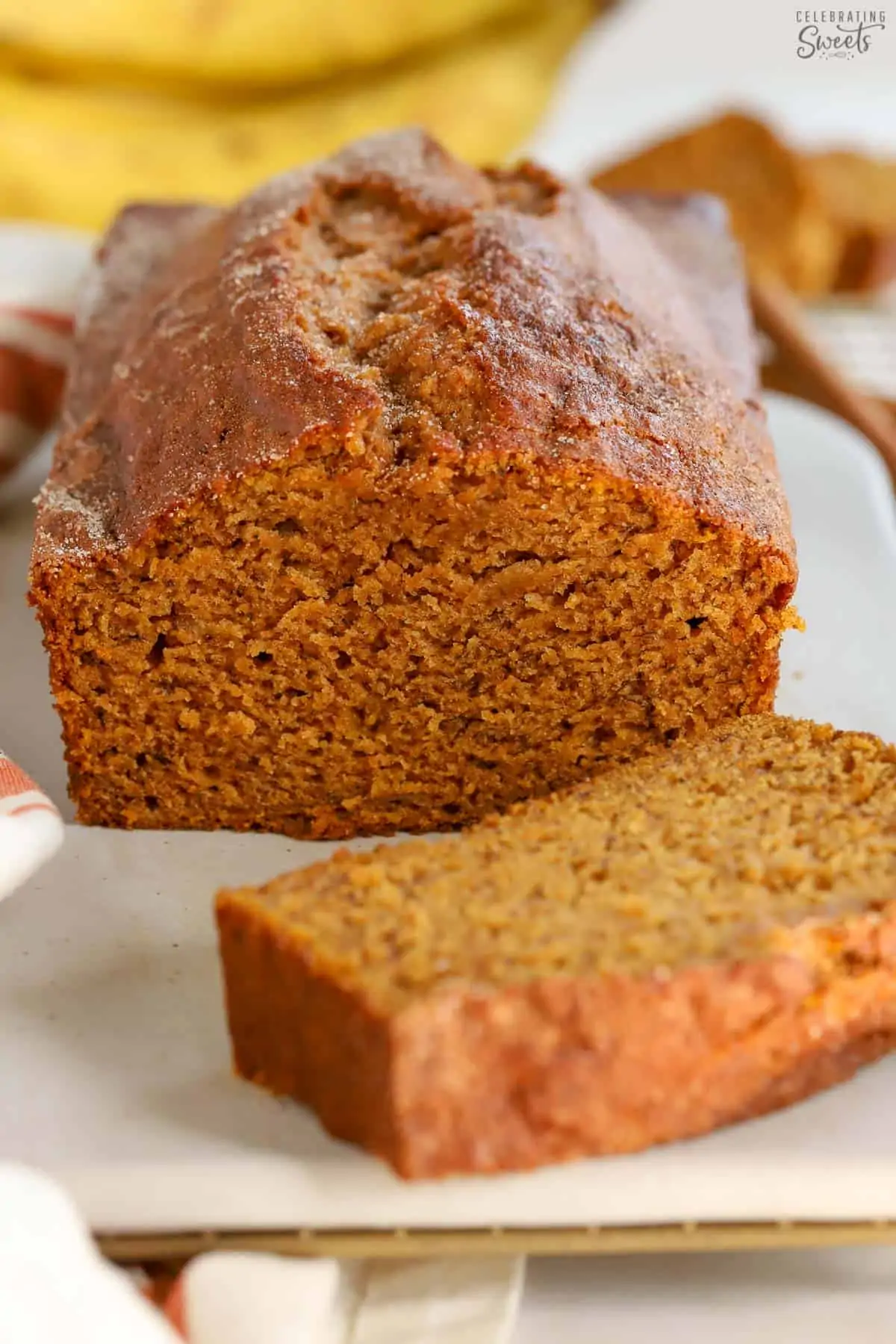 Loaf of pumpkin banana bread on a white board with bananas in the background.