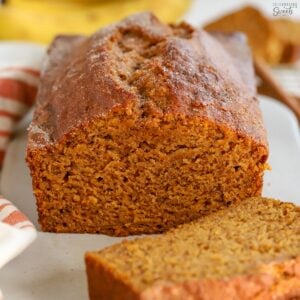 Loaf of pumpkin banana bread on a white board with bananas in the background.