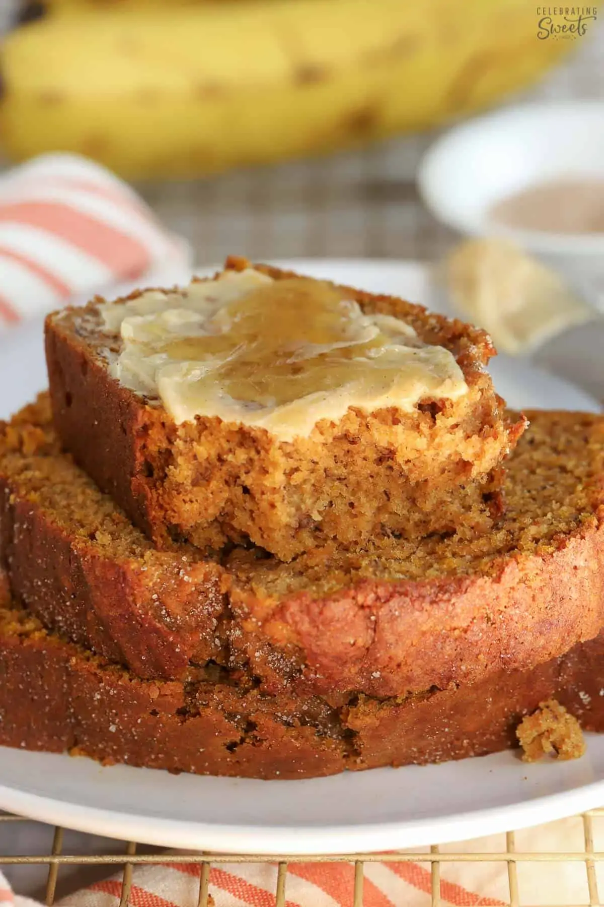 Three slices of pumpkin banana bread on a white plate with bananas in the background.