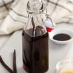 Vanilla extract in a glass container with vanilla beans next to it.
