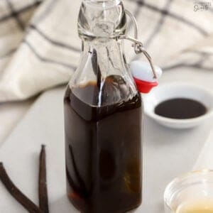Vanilla extract in a glass container with vanilla beans next to it.