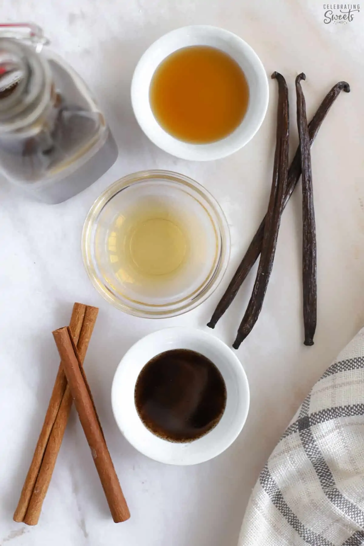 Vanilla beans, cinnamon sticks, and extracts in small bowls.