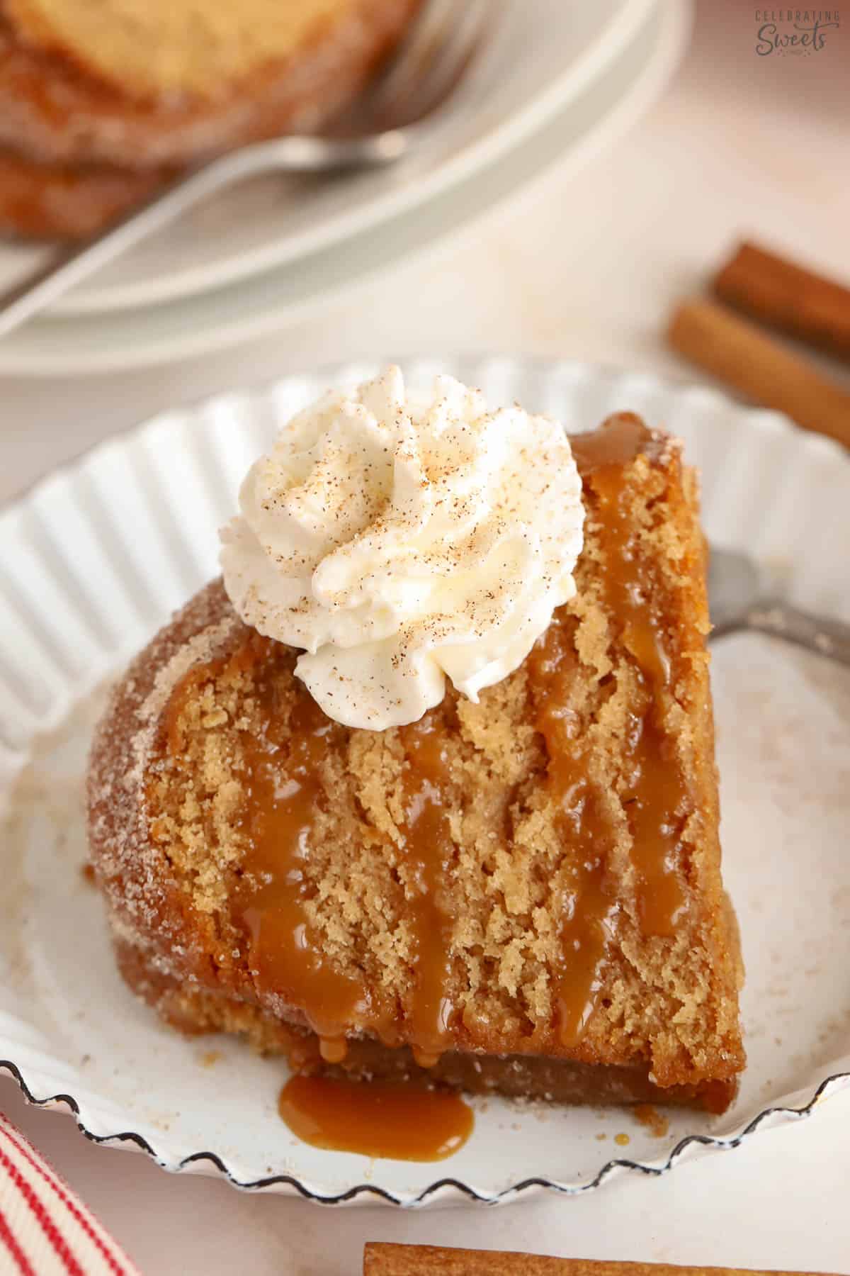 Slice of apple cider donut cake drizzled with caramel sauce and topped with whipped cream.
