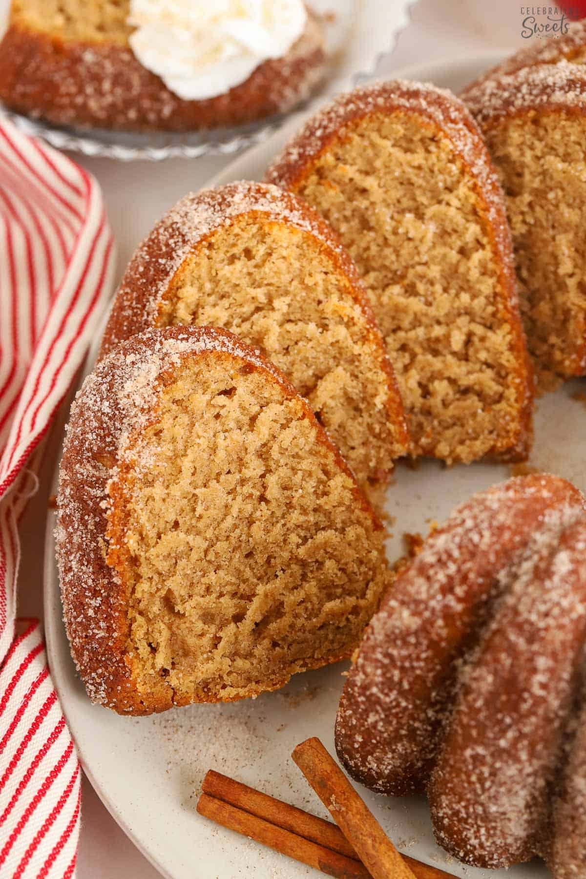 Slices of apple cider donut cake on a white platter next to a red and white striped towel.