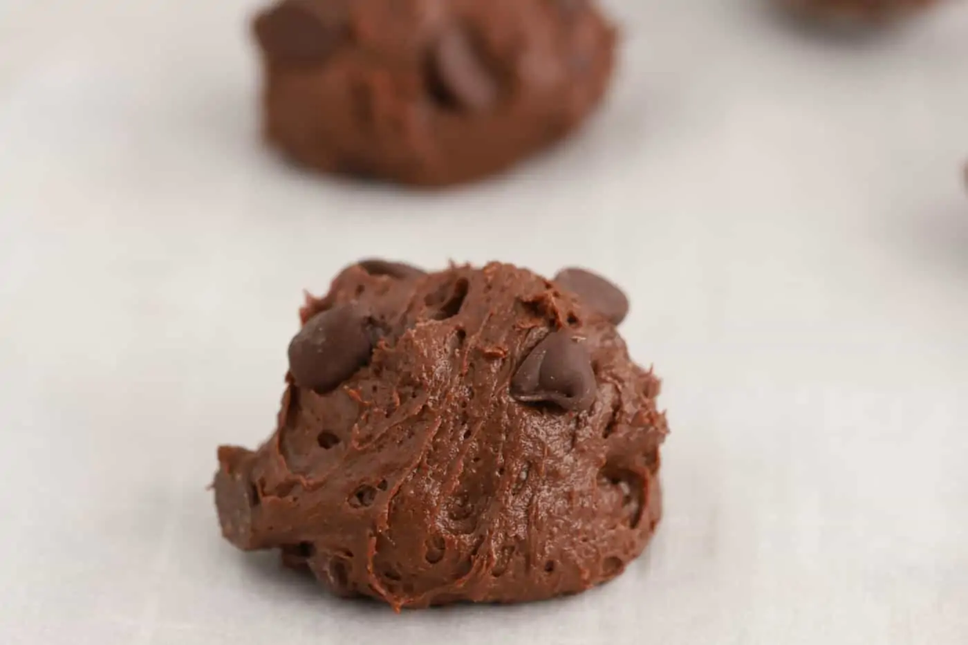 Scoop of brownie cookie dough topped with chocolate chips on a baking sheet.
