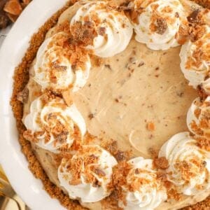 Butterfinger pie in a white pie plate topped with swirls of whipped cream.