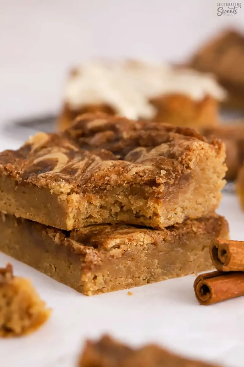 Stack of two cinnamon roll blondies next to two cinnamon sticks.