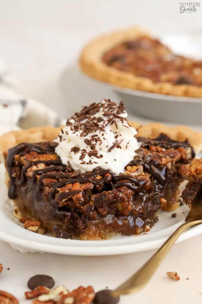 Slice of chocolate pecan pie on a white plate topped with whipped cream and chocolate sauce.
