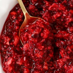 Closeup of cranberry orange relish in a white bowl with a gold spoon.