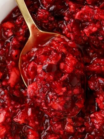 Closeup of cranberry orange relish in a white bowl with a gold spoon.