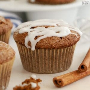 Gingerbread muffins topped with white icing next to two cinnamon sticks.
