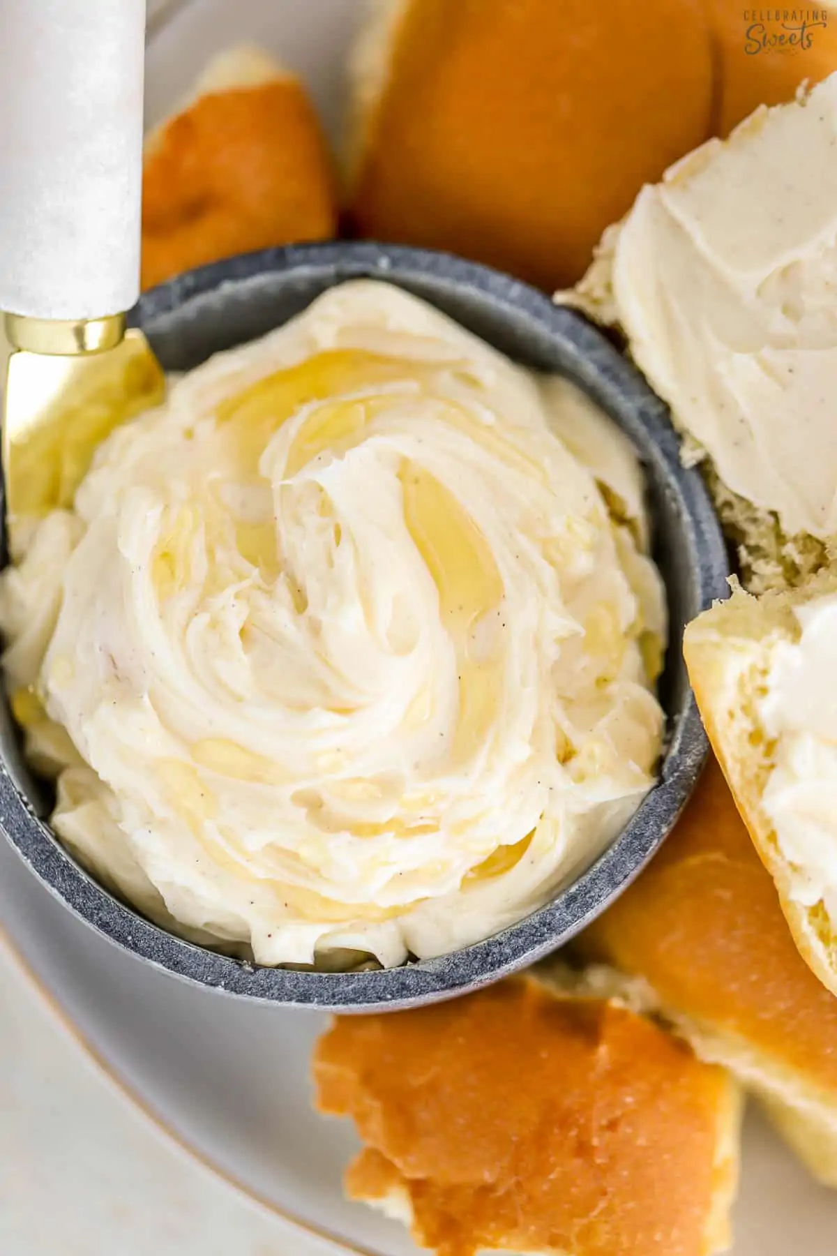 Closeup of honey butter in a blue bowl next to a plate of dinner rolls.