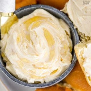 Closeup of honey butter in a blue bowl next to a plate of dinner rolls.