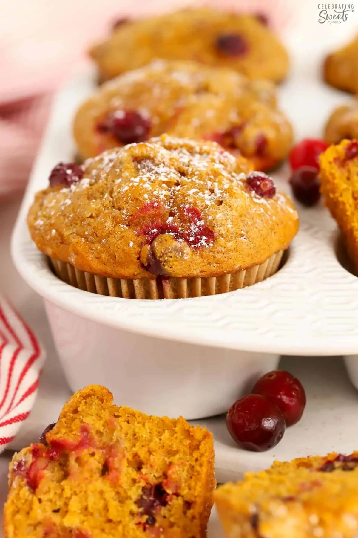 Pumpkin Cranberry Muffins in a white muffin pan next to a red and white striped towel.