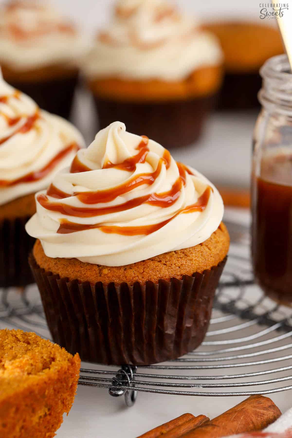 Pumpkin cupcake on a wire rack topped with white frosting and caramel.