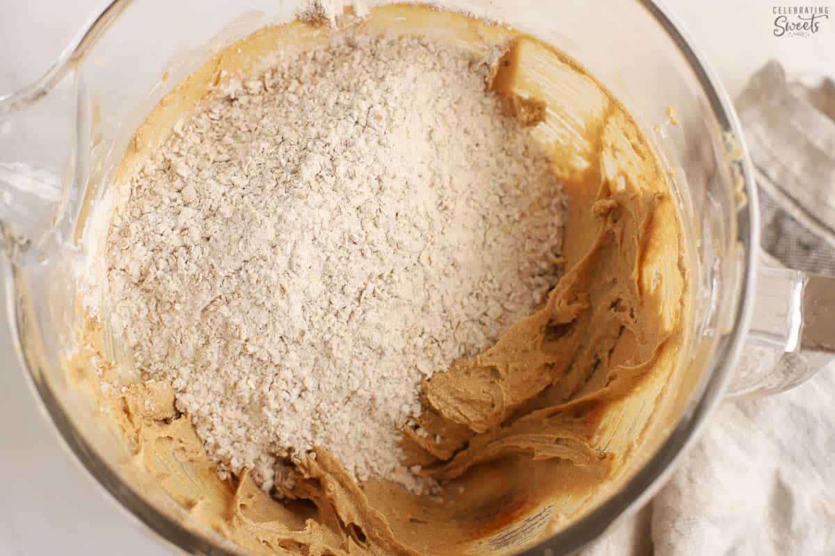 Cookie dough (brown batter, flour, oats) in a large glass bowl.