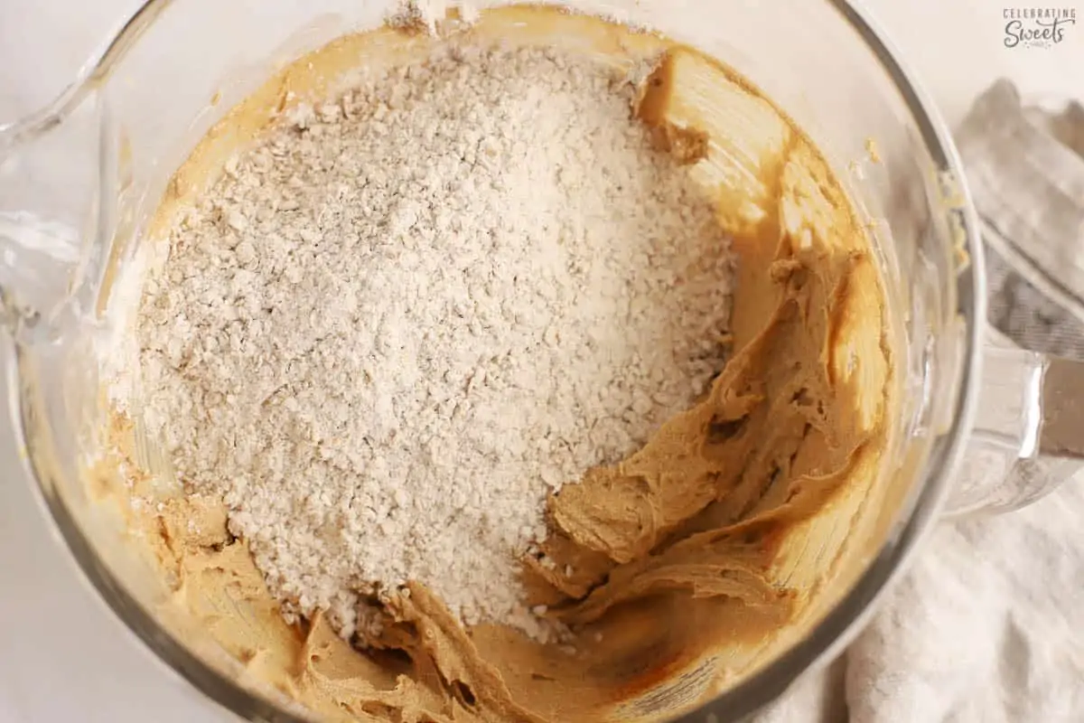 Cookie dough (brown batter, flour, oats) in a large glass bowl.