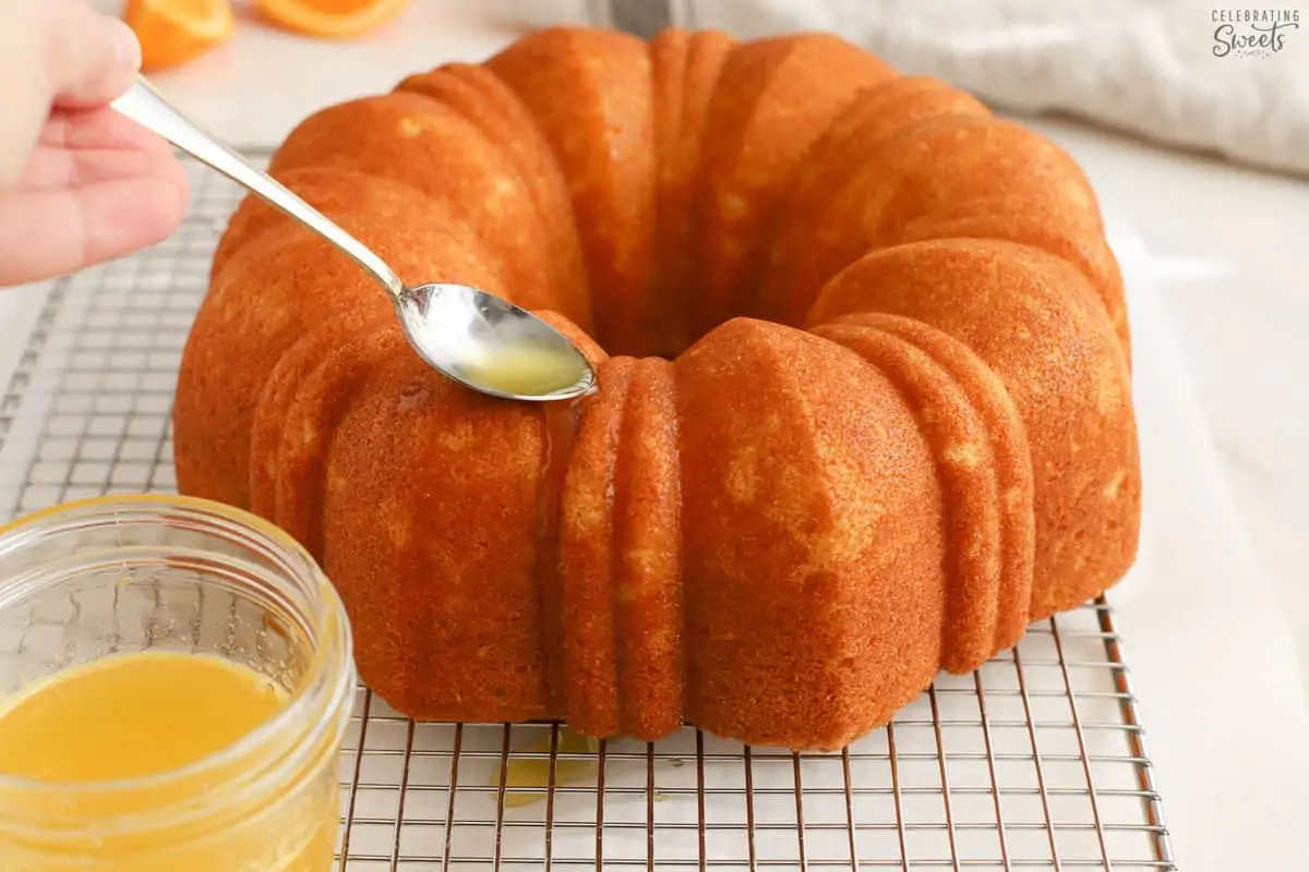 Orange syrup being spooned over an orange bundt cake.