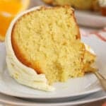 Slice of orange bundt cake on a white plate with a gold fork.