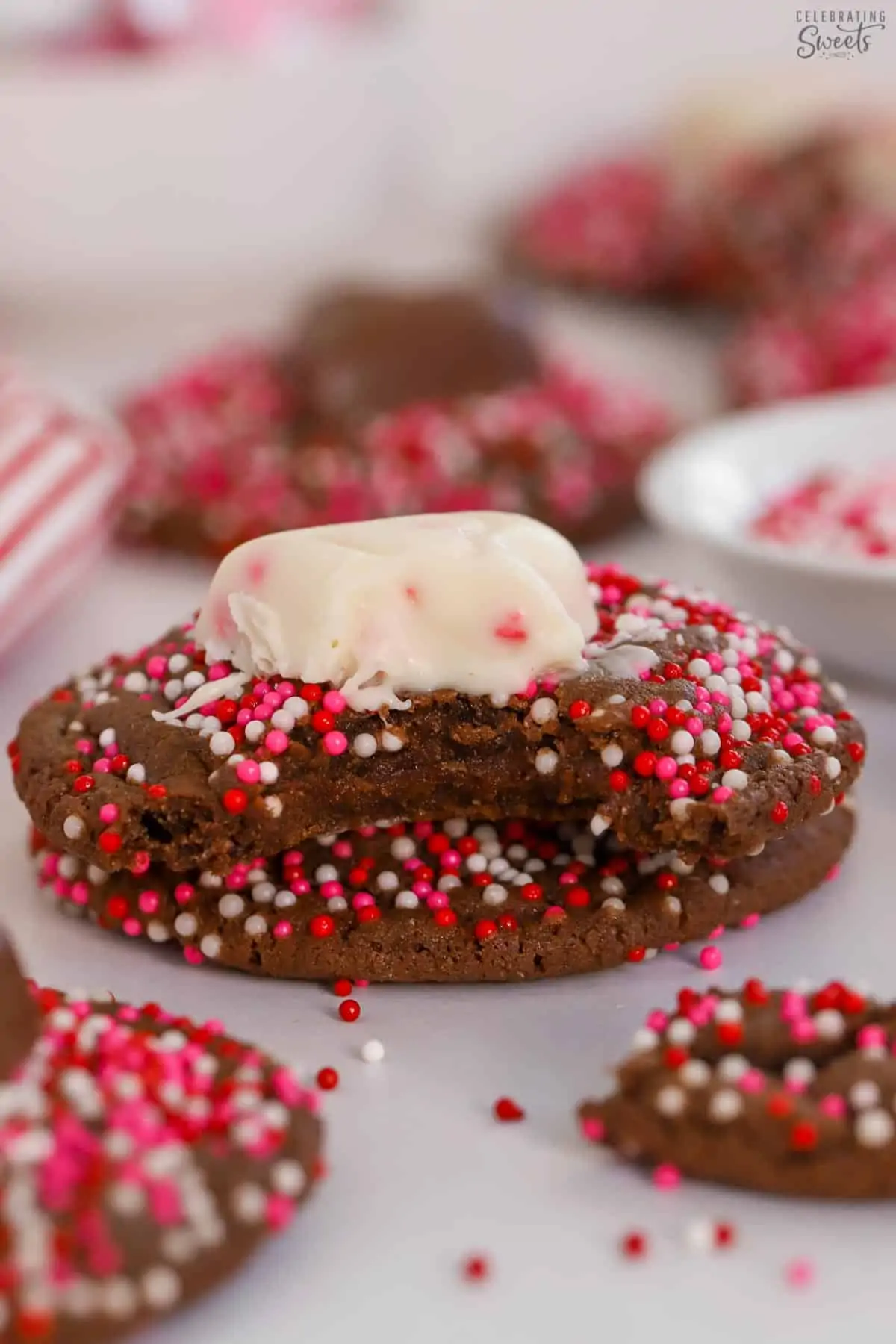 Chocolate cookies covered in red and pink sprinkles topped with chocolate hearts.