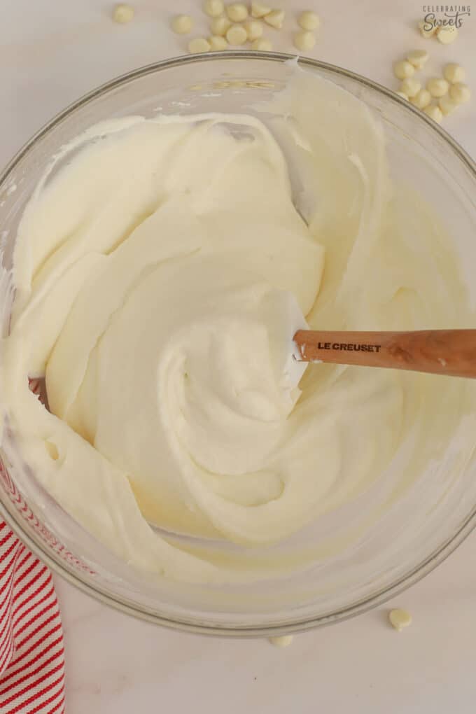 White chocolate mousse in a glass bowl with a rubber spatula.