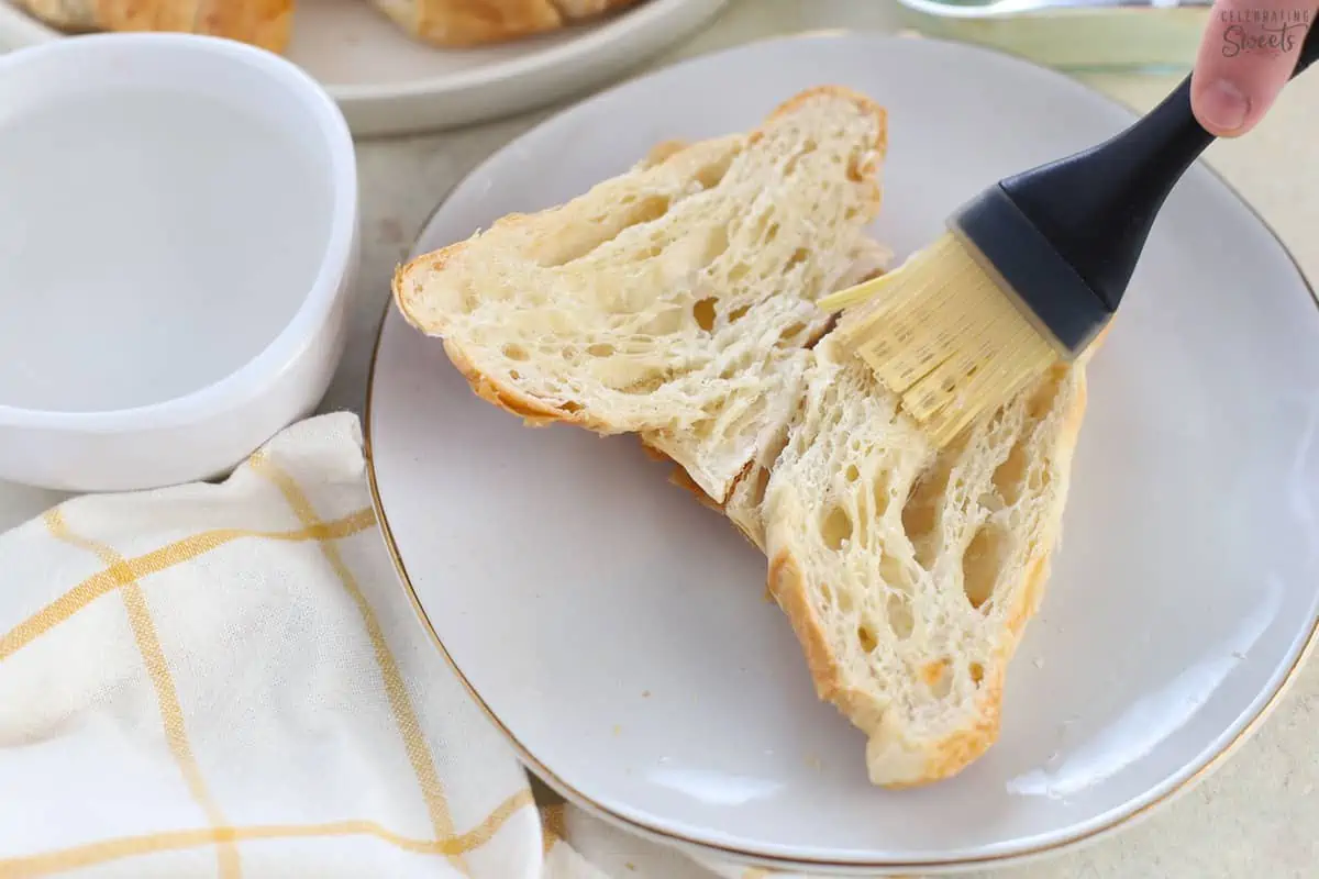Almond syrup being brushed on a halved croissant.