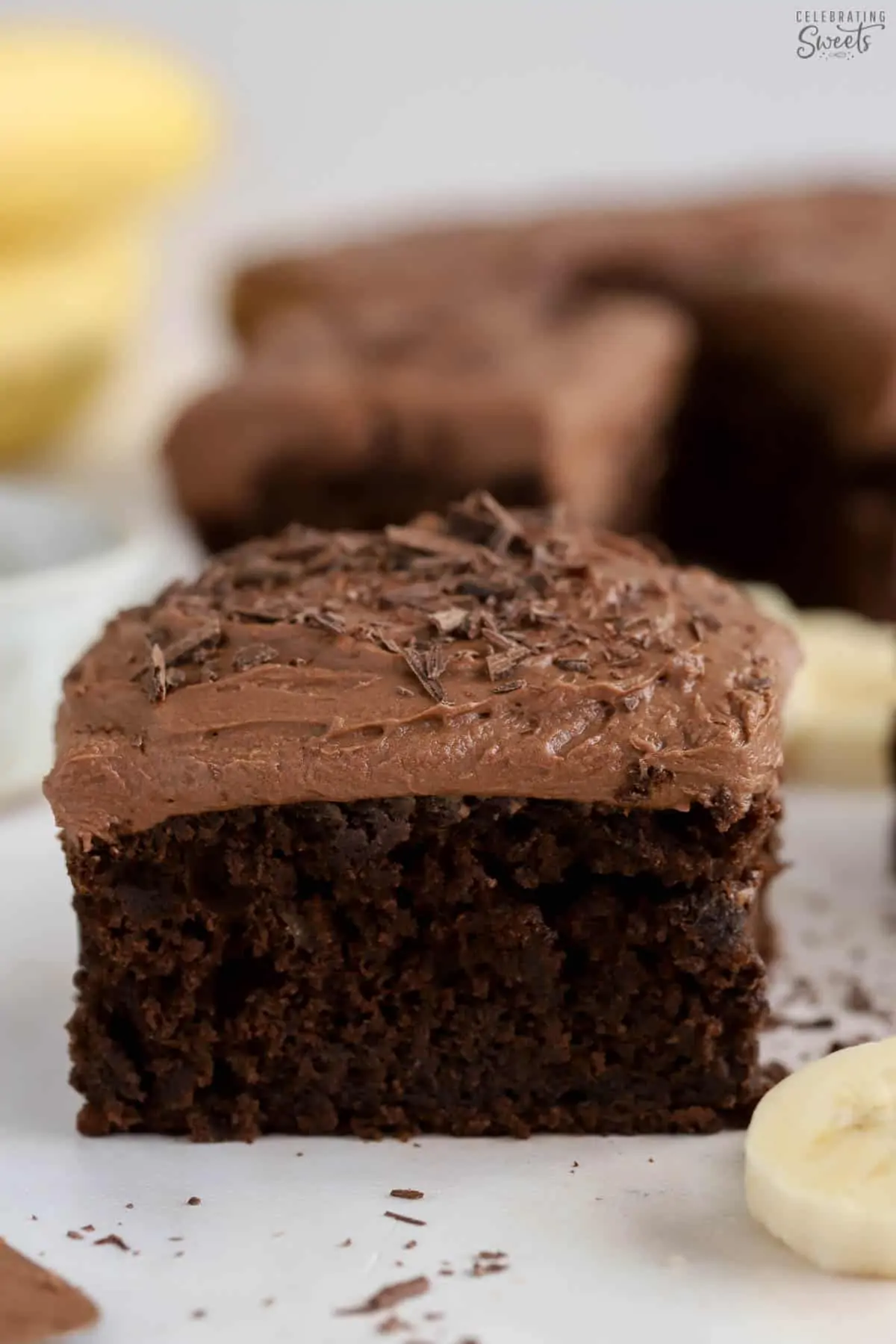 Slice of chocolate banana cake topped with chocolate frosting and chocolate shavings.