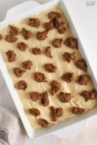 Dollops of cinnamon butter on cake batter in a white pan.
