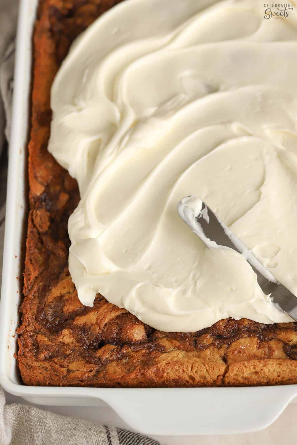 Cream cheese frosting being spread onto cinnamon cake.