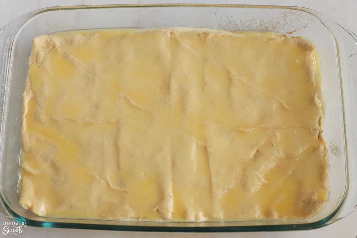 Melted butter on top of crescent roll dough in a glass pan.