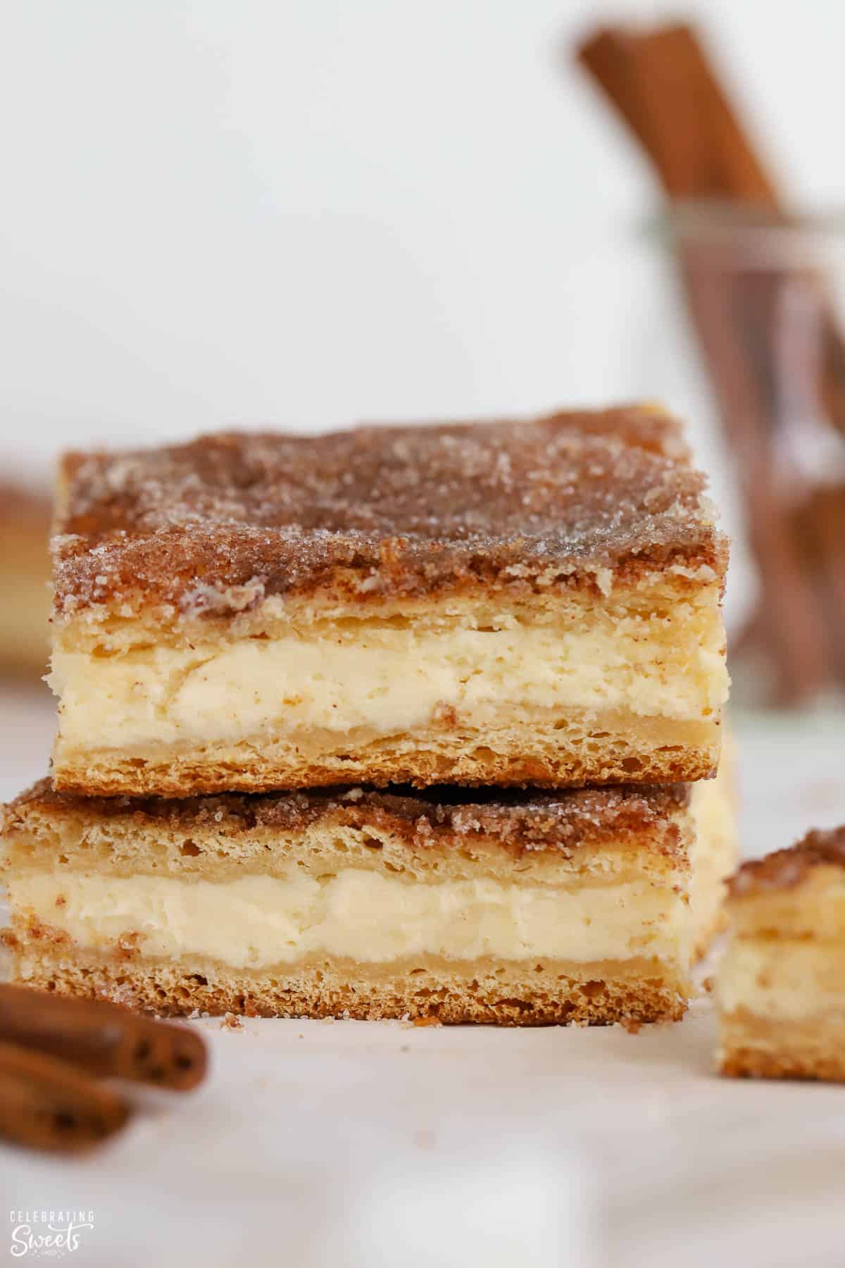 Stack of churro cheesecake bars next to cinnamon sticks.
