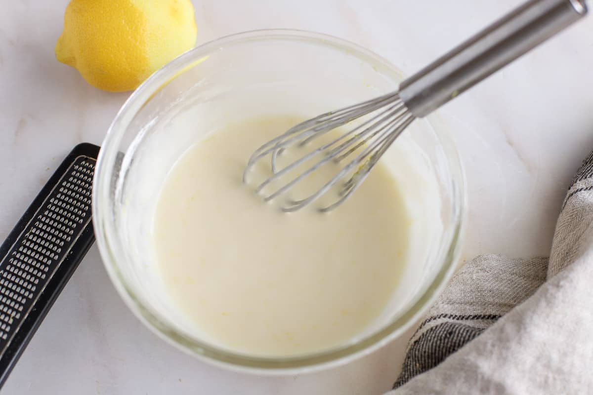 White icing in a glass bowl with a whisk.